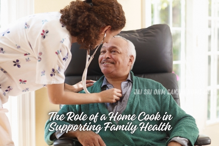 A caregiver checking the health of a smiling elderly man seated comfortably, with a home cook in the background preparing a meal. This image illustrates the vital role of a home cook in supporting family health, showcasing the services provided by Jai Sri Ohm Sakthi Home Care in Coimbatore