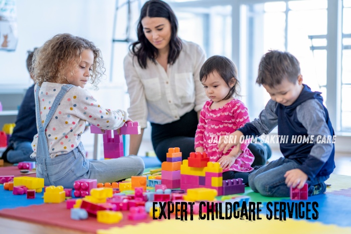 A caregiver supervising young children as they play and build structures with colorful blocks on a play mat. This image represents expert childcare services provided by Jai Sri Ohm Sakthi Home Care in Coimbatore